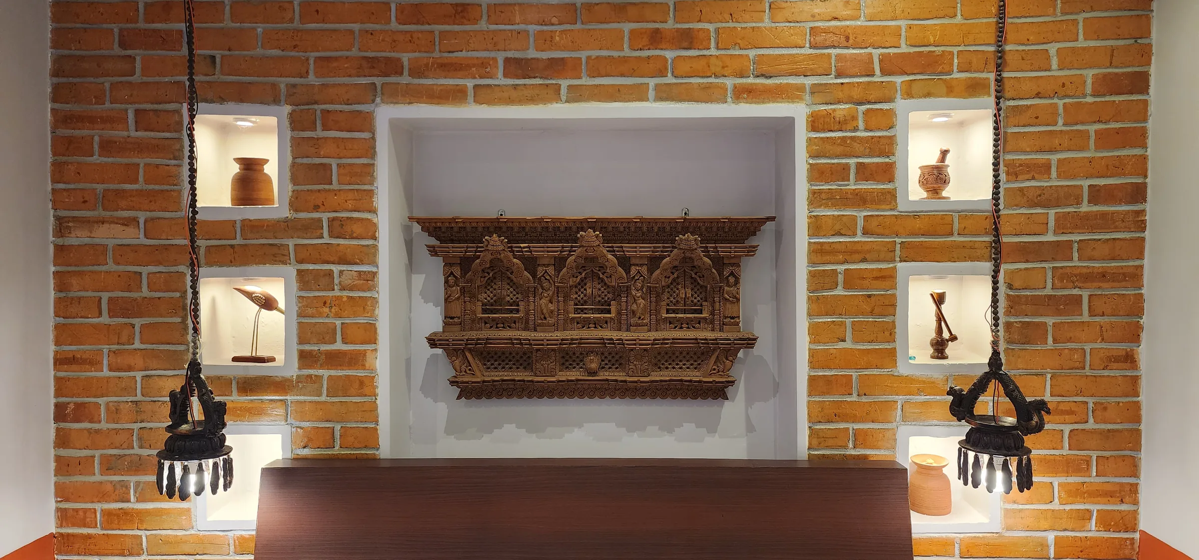 A triple carved Newari sha-jyaal window displayed in a brick alcove with traditional pottery and oil lamps